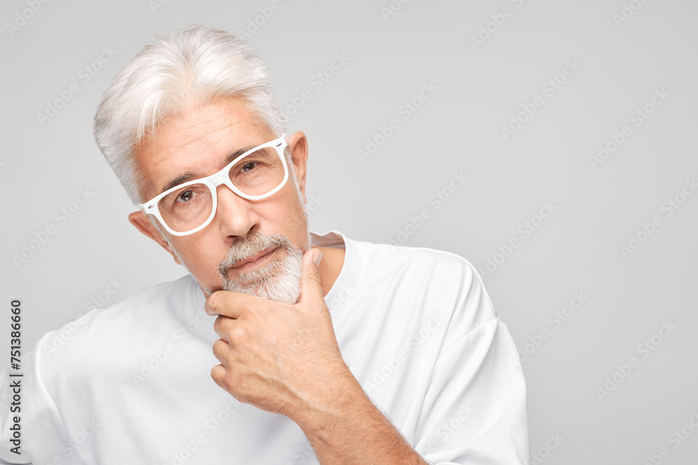 Mature man with white hair and glasses looking thoughtful against a gray background. Mature man with white hair and glasses looking thoughtful against a gray background.
