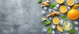 Juicy oranges, zesty lemons, fragrant gingers, and refreshing mints sit atop ice cubes, ready to enhance a tasty ginger ale. The ingredients are neatly arranged on a grey wooden table.