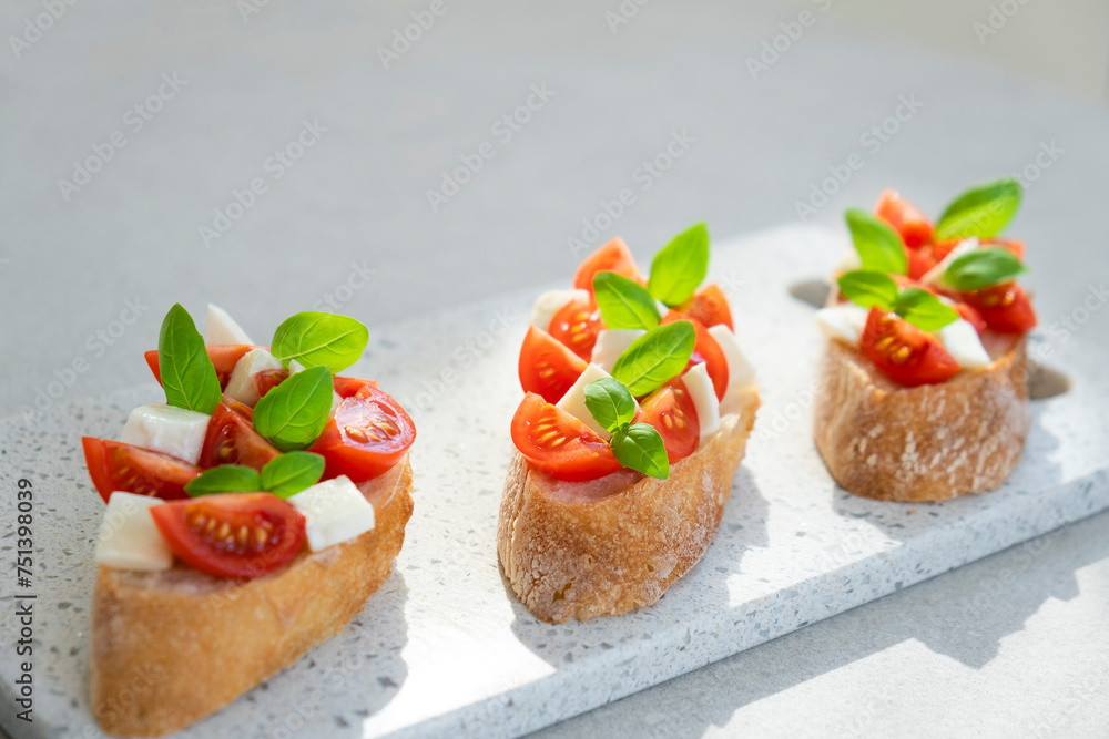 Bruschetta with cherry tomatoes, mozzarella cheese and basil in sun rays on marble board. Traditional Italian appetizer, snack or antipasto. Vegetarian food. Healthy eating. Mediterranean food. Bruschetta with cherry tomatoes, mozzarella cheese and basil in sun rays on marble board. Traditional Italian appetizer, snack or antipasto. Vegetarian food. Healthy eating. Mediterranean food.
