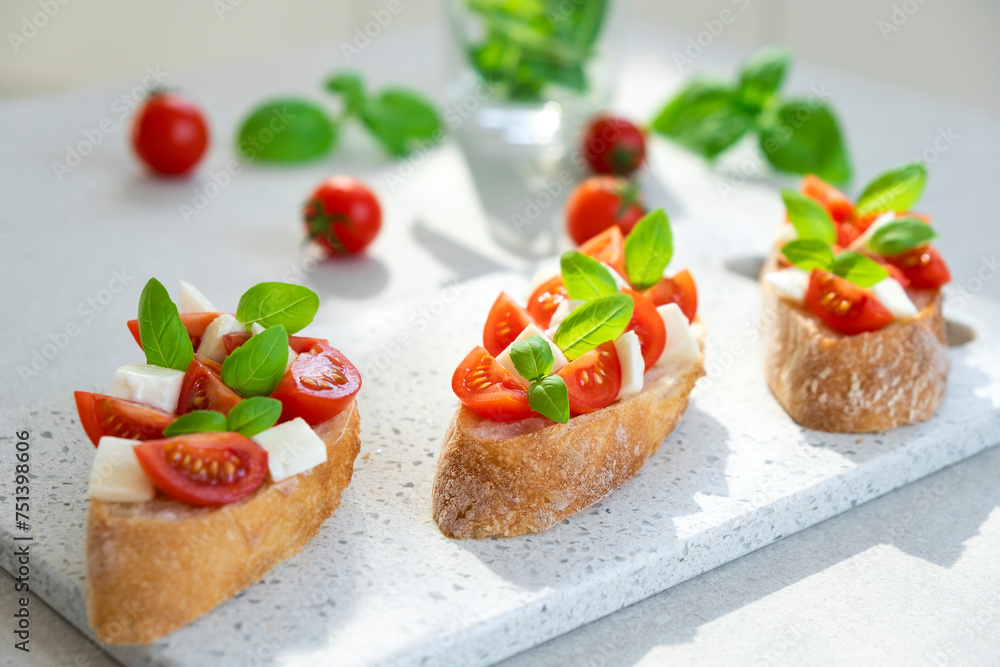 Caprese bruschetta with tomatoes, mozzarella cheese and basil in sun rays on marble board. Traditional Italian appetizer, snack or antipasto. Vegetarian food. Healthy eating. Mediterranean food.