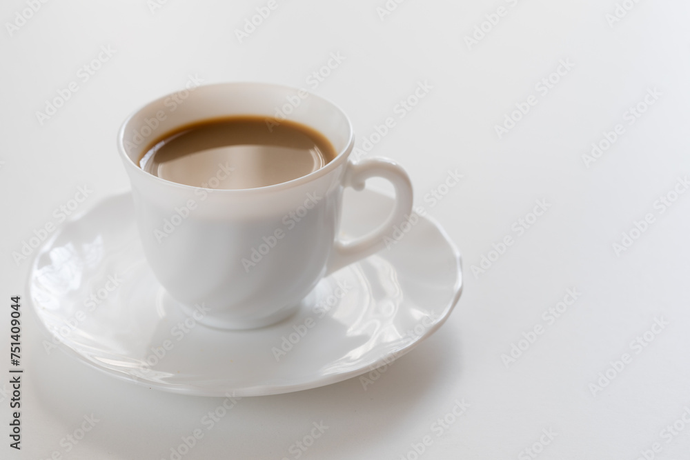 Tazzina bianca con caffè e piattino su tavolo bianco