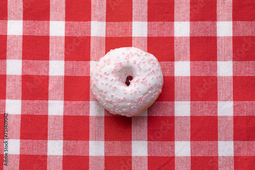 Ciambella con glassa e zuccherini rosa su tovaglia a quadretti bianchi e rossi photo
