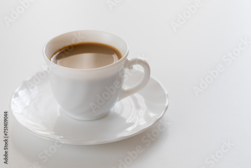 Tazzina bianca con caffè e piattino su tavolo bianco photo