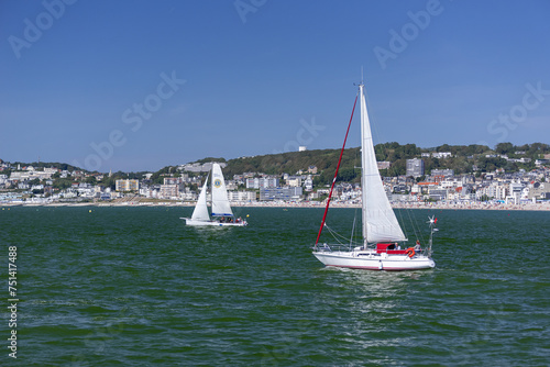 Focus on small leisure sailboats which navigate in English Channel with the town of Le Havre and its pebble beach in the background.