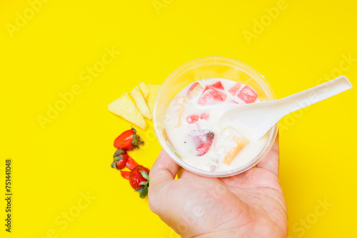 es buah or sup buah is indonesian fruit cocktail ice desert, contains strawberry, pineapple, and other tropical fruits mixed with ice cube, and condensed milk. isolated on yellow background. photo