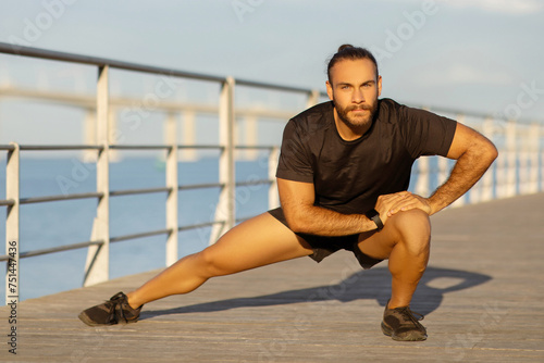 Fit and motivated sporty guy showcases deep lunge exercise outside