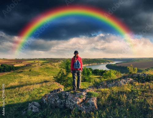 Tourist standing on the edge of the cliff and looking at the rainbow. Rainbow over the river. Nature of Ukraine © sergnester