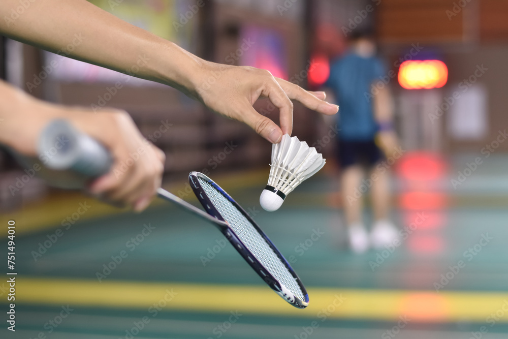 Fototapeta premium Badminton player holds racket and white cream shuttlecock in front of the net before serving it to another side of the court, soft focus.