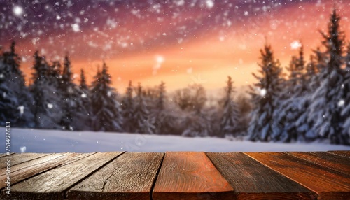dark wooden table for product montage set against a blurry snowy landscape with silhouette trees under an orange and pink sky during sunrise or sunset complete with falling snowflakes © Wayne