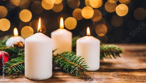 christmas decoration with white burning candles on wooden table against bokeh light background