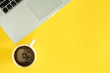 Cup of coffee and laptop on a yellow background, flat lay.