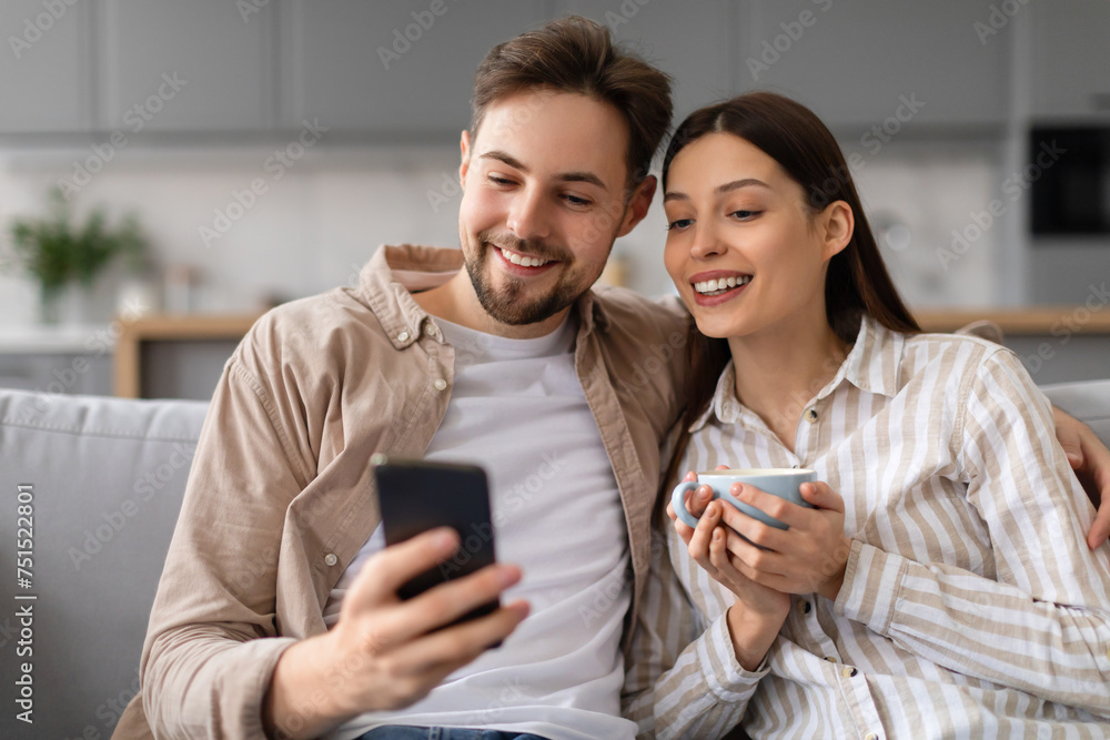 Spouses smiling at phone with coffee on couch Spouses smiling at phone with coffee on couch