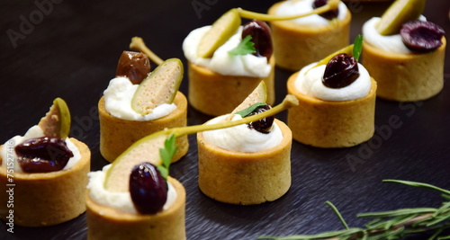 Antipasto with olives, small appetizers and tartlets on a black platter with cream cheese filling and black olives, cold appetizer at the buffet