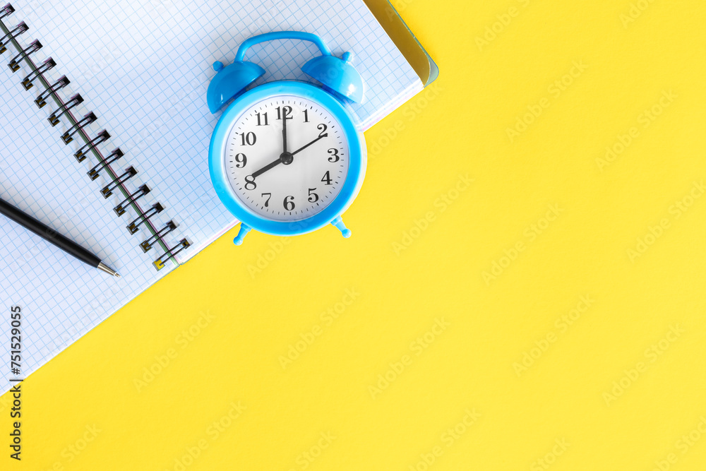 Blue alarm clock and notepad on a yellow background, flat design. Blue alarm clock and notepad on a yellow background, flat design.