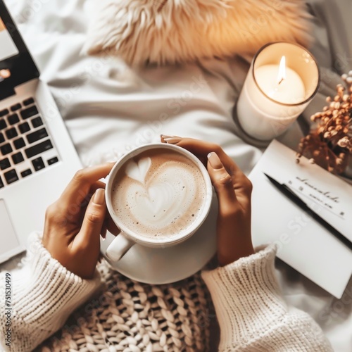 women's hand holding a coffee cup in front of a laptop with candles next to it, in the style of effortlessly chic, brown and beige, dreamy, warmcore, valentine hugo, life in new york city