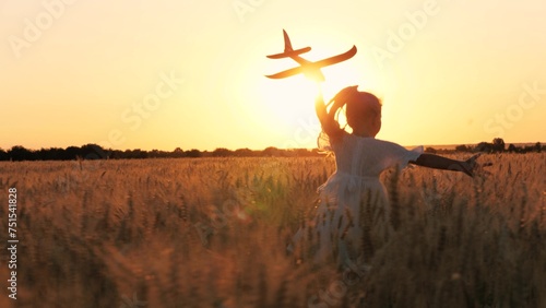 Adorable female kid silhouette running with aircraft toy at cinematic sunset sunrise wheat field back view. Happy little girl child playing pilot game with plane plaything enjoy childhood at dusk