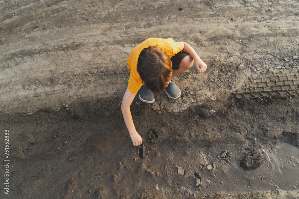Portrait of a boy in nature. A boy in an orange T-shirt plays with mud in the ground in nature. Happy child, lifestyle. Candid Portraits. Portrait of a boy in nature. A boy in an orange T-shirt plays with mud in the ground in nature. Happy child, lifestyle. Candid Portraits.