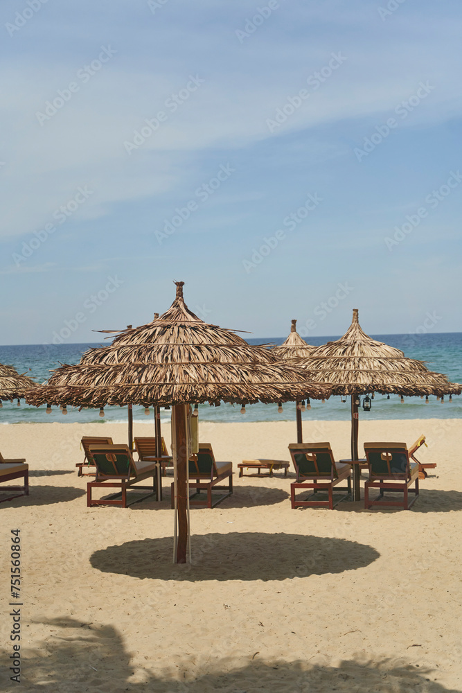 Naklejka premium Straw sunshades and sunbeds on the empty pebble beach with sea in the background. Deserted beach with rattan sun loungers and umbrellas