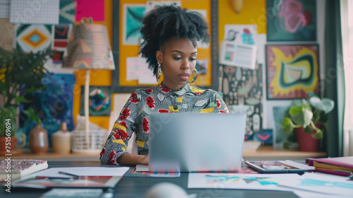 A young black graphic designer creating artwork on her laptop, in an artistic office surrounded by digital tablets and design tools, business technology, with copy space