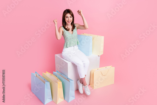 Photo of overjoyed happy cute girl wear trendy clothes sitting with raised hands shouting yes hooray isolated on pink color background