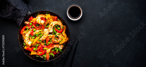 Hot stir fry shrimps with colorful paprika, green peas, chives and sesame seeds with ginger, garlic and soy sauce. Black kitchen table background, top view