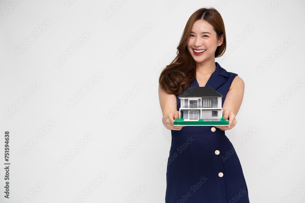 Young Asian woman smiling and holding house sample model isolated over white background, Real estate and home insurance concept Young Asian woman smiling and holding house sample model isolated over white background, Real estate and home insurance concept