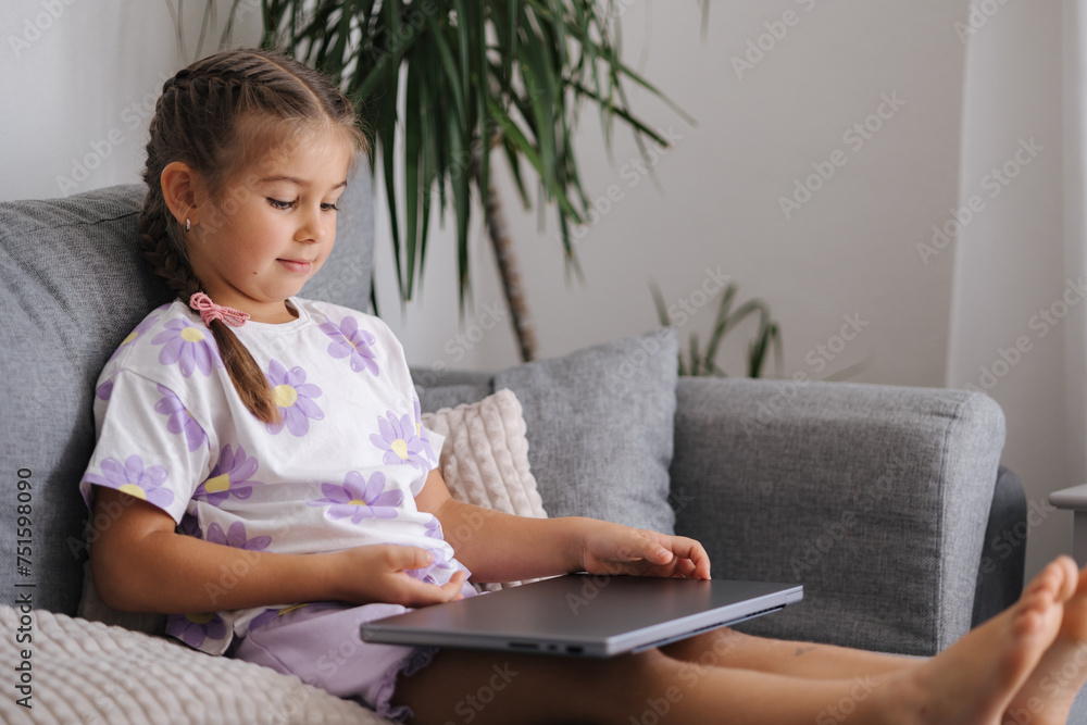Smart little girl open gray laptop while she sitting on sofa at home Smart little girl open gray laptop while she sitting on sofa at home