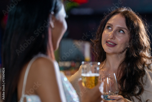 two girls in sexy dress are drinking and dancing at bar. Dance party with group people dancing . Women and men have fun and drinking martini cocktail in night club.