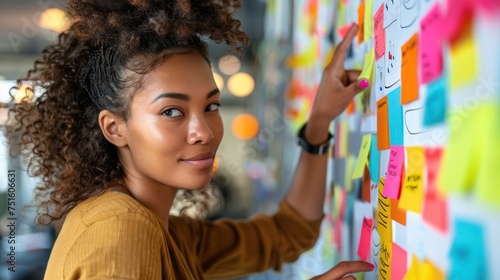 A young female marketing professional is brainstorming using colorful sticky notes on a white wall.