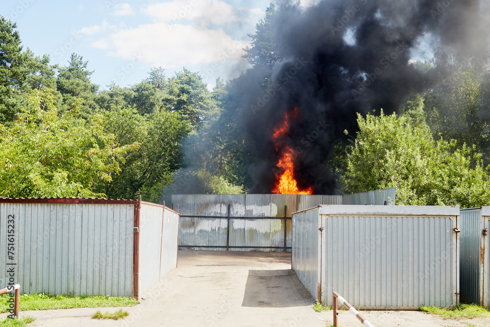 Fototapeta premium Big fire and black smoke behind fence made of corrugated steel sheets