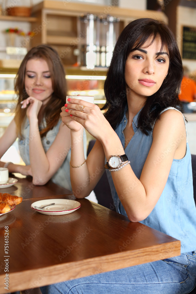 Two young women sit at table in cafe with tea, focus on right girl