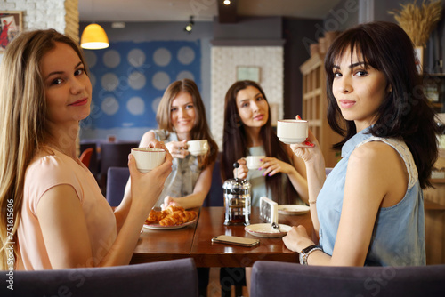 Four beautiful women sit in cafe and drink tea, focus on right girl
