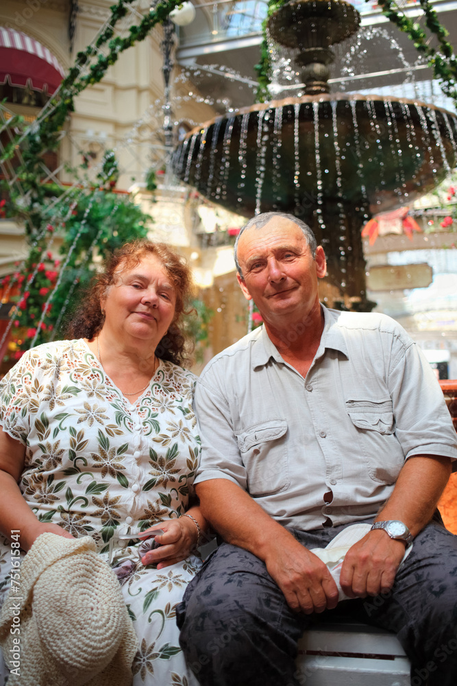 Elderly couple with lovely smiles sitting in front of fountain in shopping centre Elderly couple with lovely smiles sitting in front of fountain in shopping centre