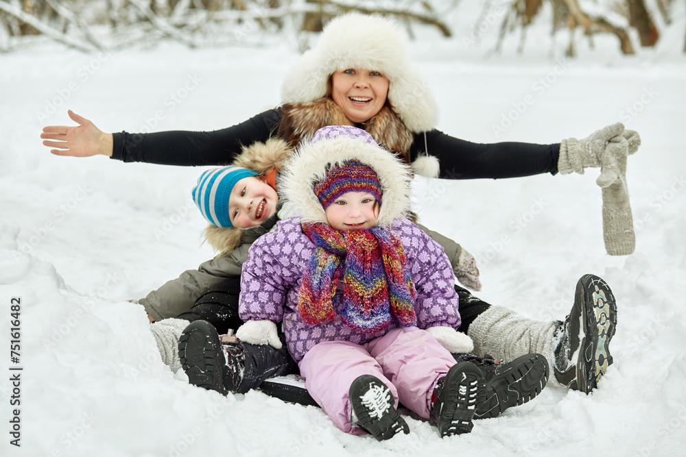 Mother and two children sit on soft sledges in winter park, focus on girl