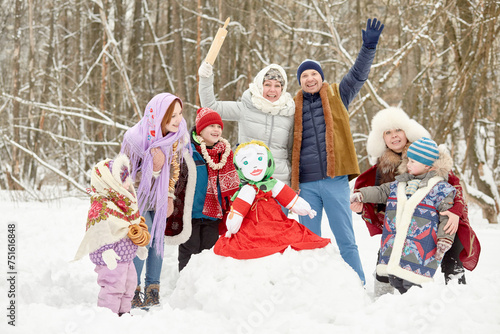 Three adults and four children around stuffed dummy Maslenitsa in winter park photo