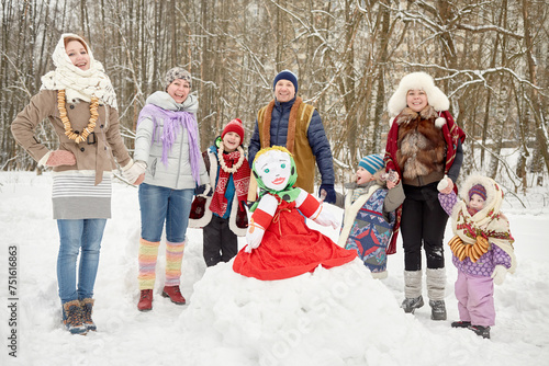 Three adults and four children stand holding hands around stuffed dummy Maslenitsa in winter park photo