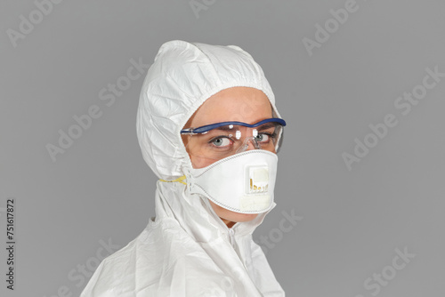 Headshot of woman in white protective suit of synthetic paper, glasses and respiritory half mask, looking at us, on gray background