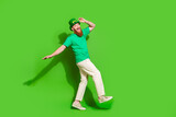 Full size photo of crazy funky young person hand touch hat dance walk isolated on green color background