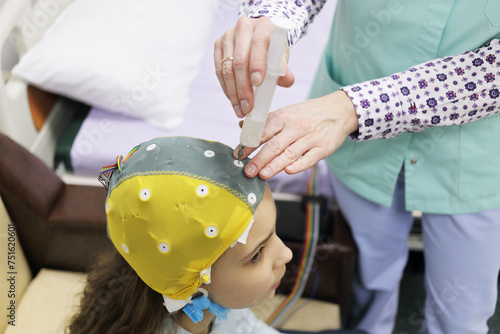 Girl before procedure electroencephalography, nurse using syringe introduces special gel for electrodes located in cap of electroencephalogram photo