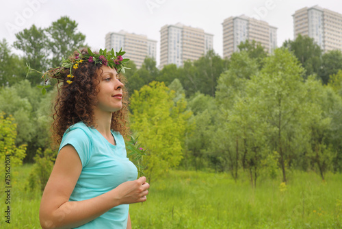 Half length portrait of young woman with wreath of flowers urban wooded area near apartment complex, holding clover photo in profile