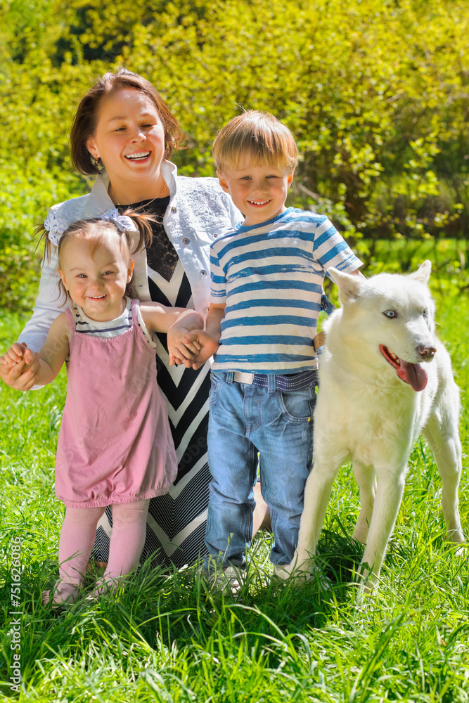 Obraz premium Mom with her daughter and son sitting with dog on grass in park
