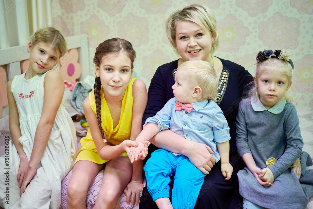 Smiling woman and four children sit on couch in room Smiling woman and four children sit on couch in room