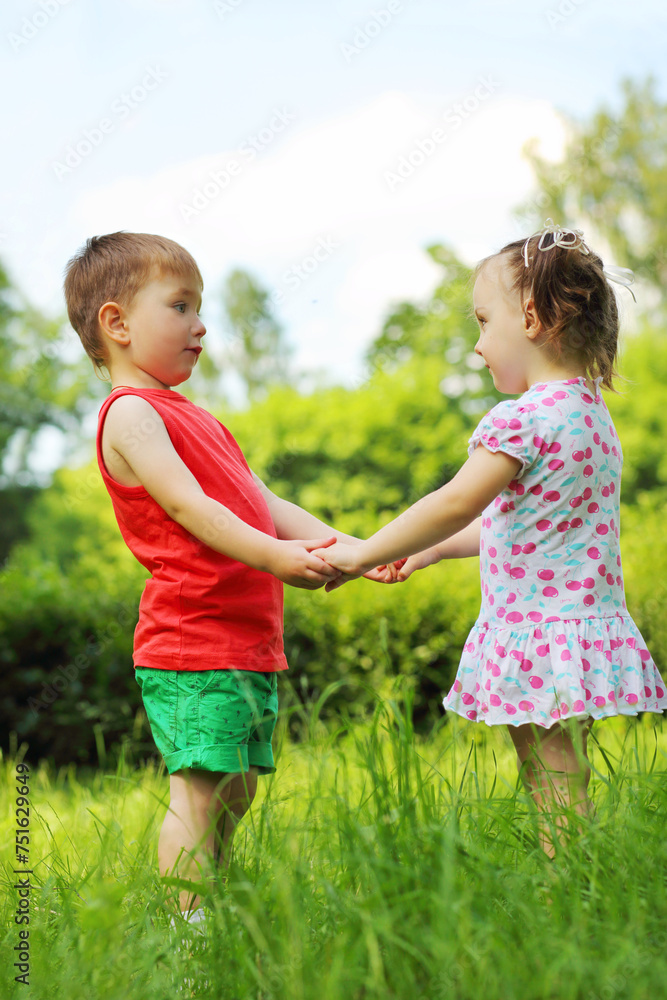 Fototapeta premium Little girl and boy hold hands on fresh green grass in park