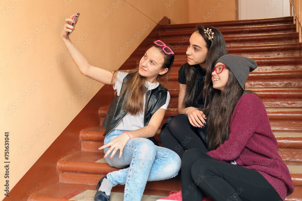 © Pavel Losevsky - Three girls make selfie photo phone on stairs at school, look in phones camera