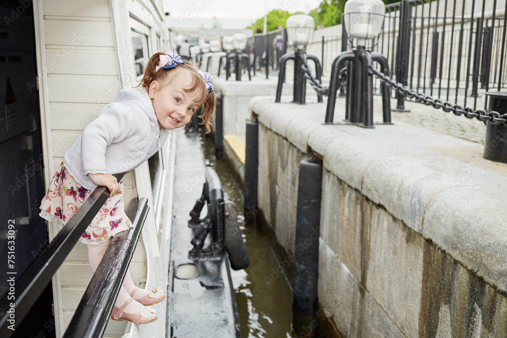 Little girl stands holding on railing at pleasure boat deck while boat approach pier