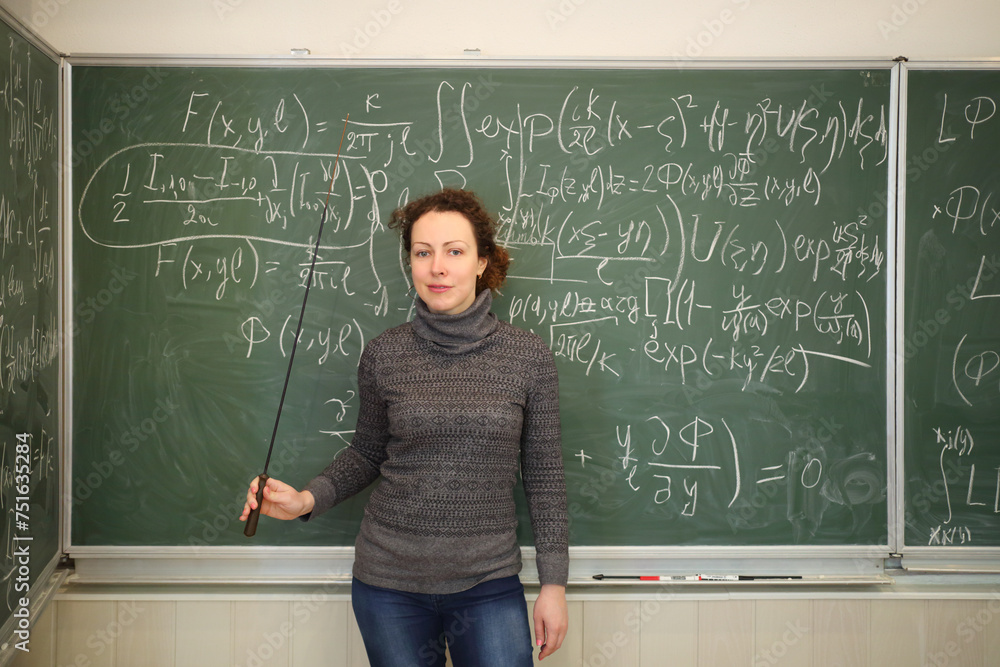 Teacher with pointer stands near blackboard with mathematics formulas in school classroom Teacher with pointer stands near blackboard with mathematics formulas in school classroom