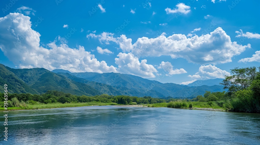 Rugged mountain terrain meeting a calm river under a spotless blue sky, creating a pristine natural panorama.