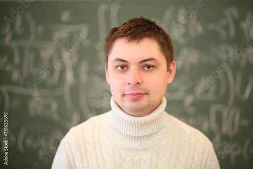 Teacher in white stands near blackboard with mathematics formulas in classroom