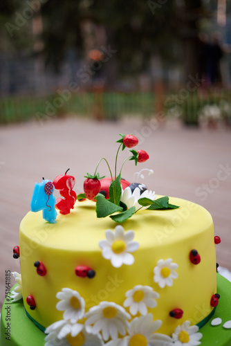 Big cake covered with yellow and green icing and decorated with camomilles and strawberries photo