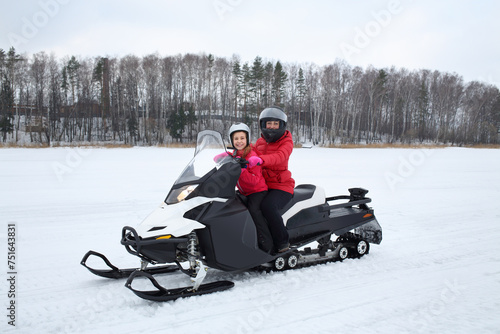 Mother with girl in helmets sitting behind the wheel of a snowmobile